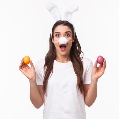 Easter party begins. Portrait of funny and cute, silly young caucasian woman celebrating divine day, wear rabbit ears and nose, holding colored eggs, gasping amused, white background.