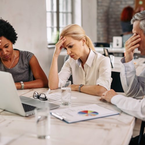 Group of business colleagues having a headache while working on laptop and trying to solve the problems during a meeting.