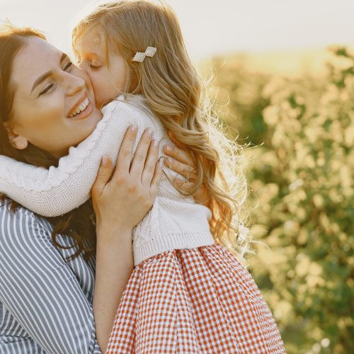 Pregnant mother and daughter. Little girl child in the summer meadow. Woman in a blue dress.