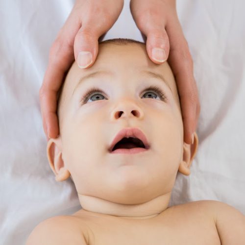 Hands of a mother touching head of her baby boy at home