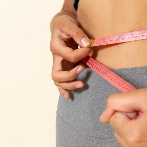 front close view young female with fit body in blue shirt measuring her waist on light white background sport health athlete workout exercise
