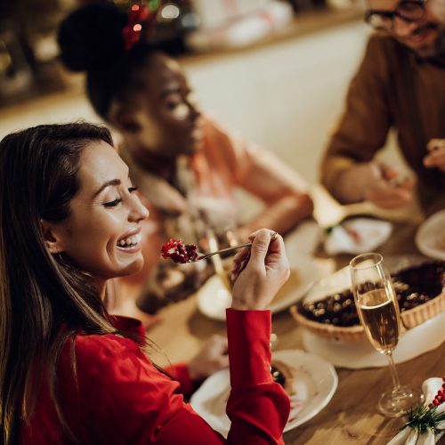 Cheerful woman eating cranberry pie while celebrating Christmas with friends in dining room.